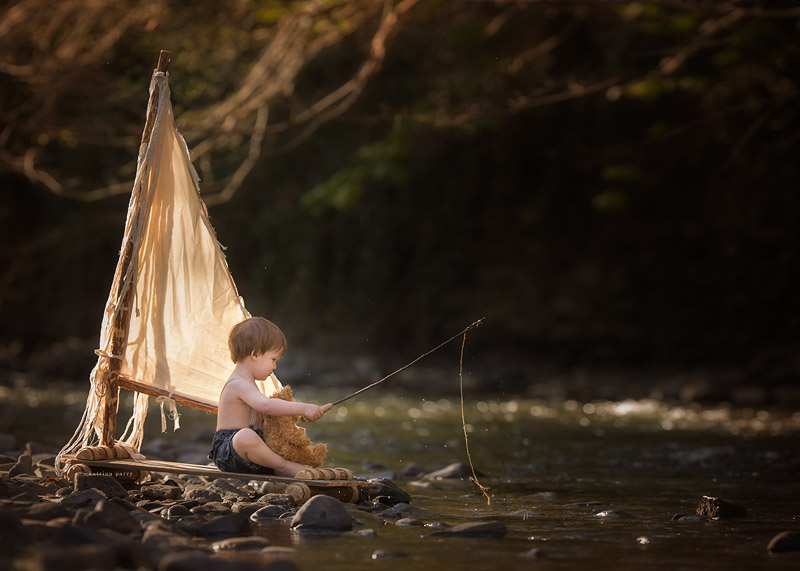 Little boy on a raft, fishing with his teddy bear.