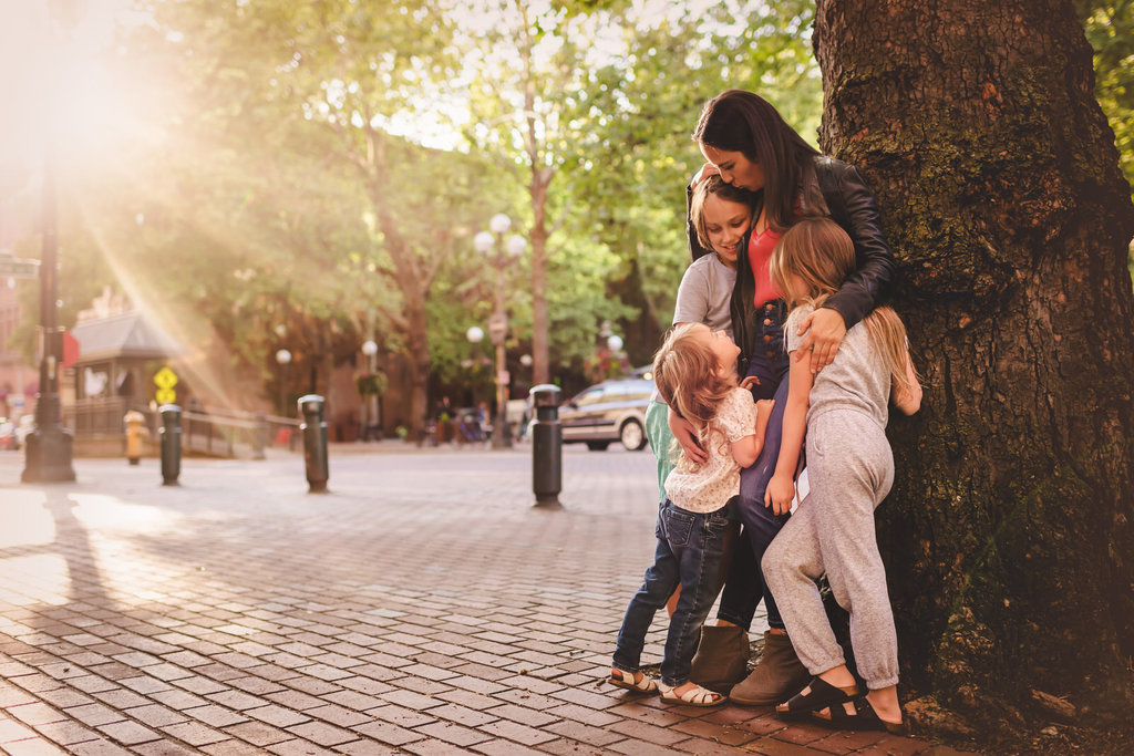 mom hugging three kids while standing against a tree in an urban setting