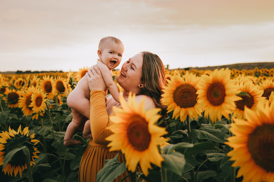 mom holding up naked baby in sunflower field