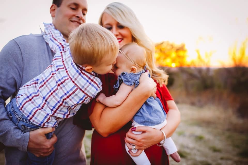 brother leaning over and kissing baby in family photograph