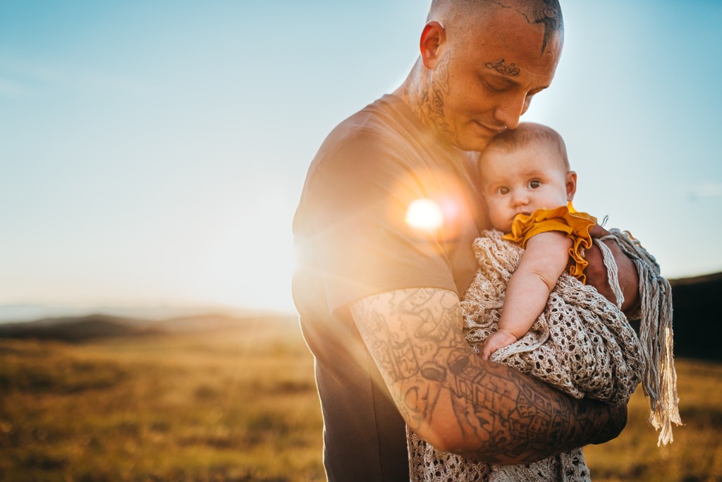 tattooed father with baby in arms at sunset