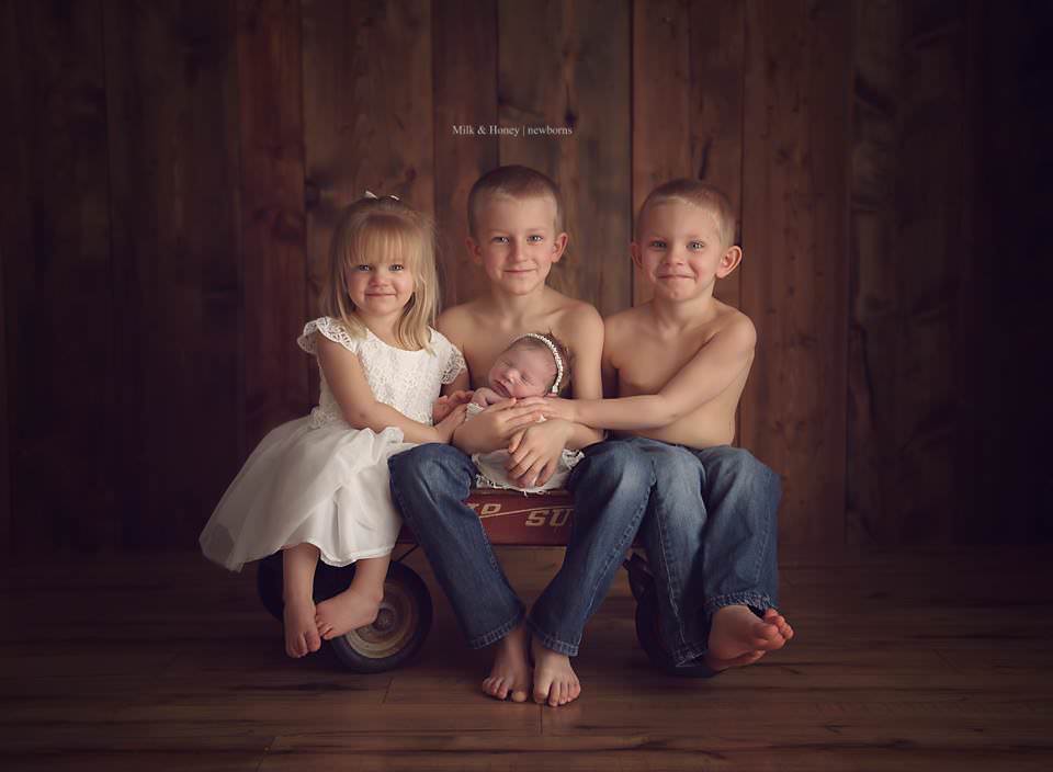 3 siblings posing in wagon with baby