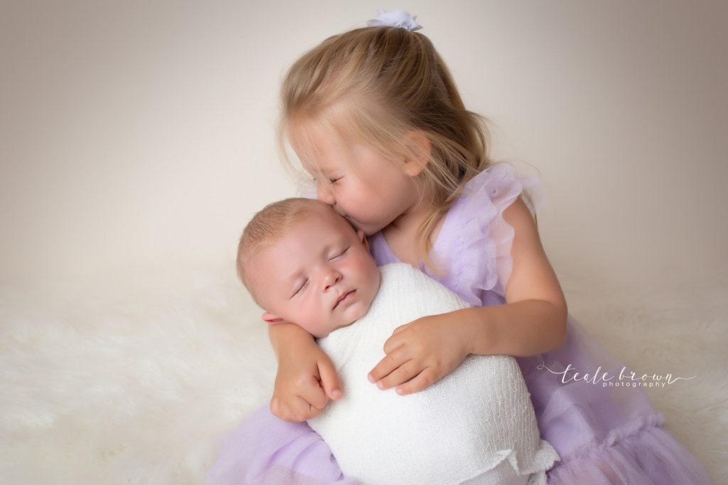 wrapped baby held by older sister
