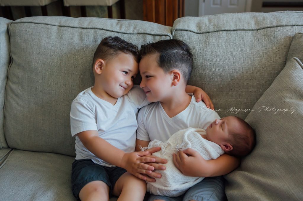 lifestyle sibling poses of two boys and newborn on couch