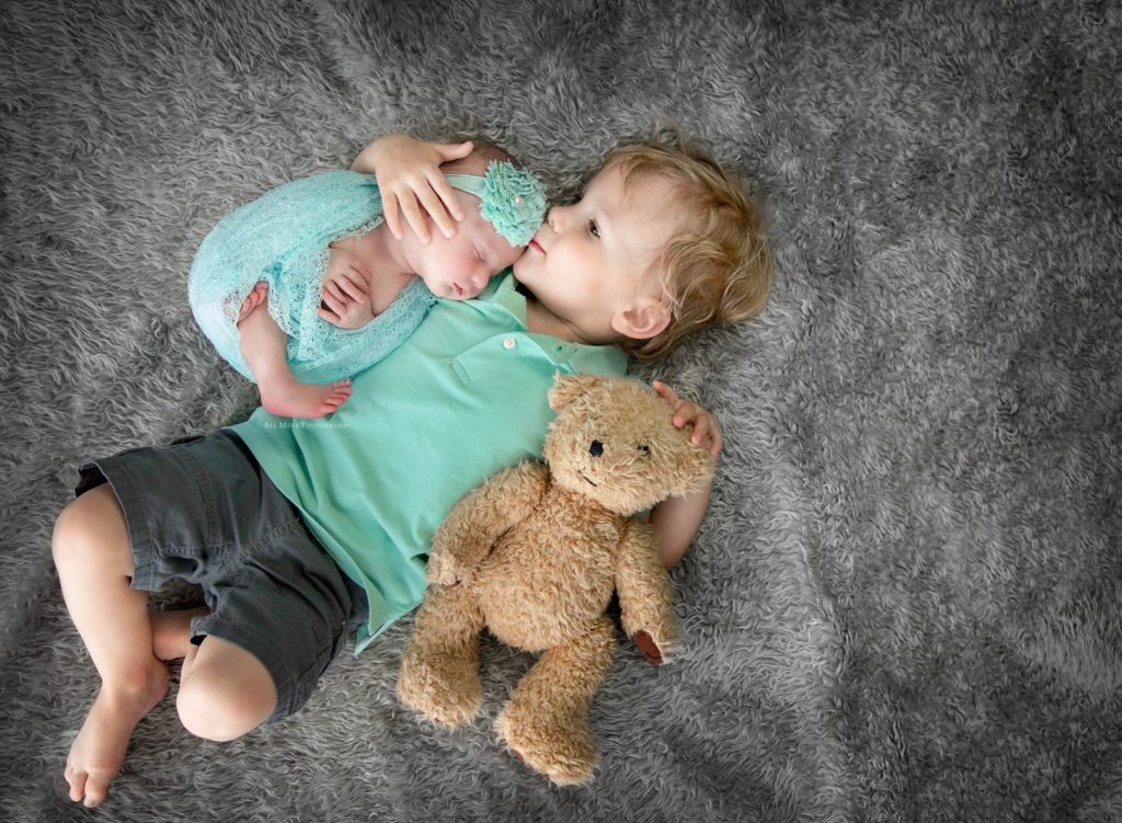 boy lying down with newborn and teddy bear