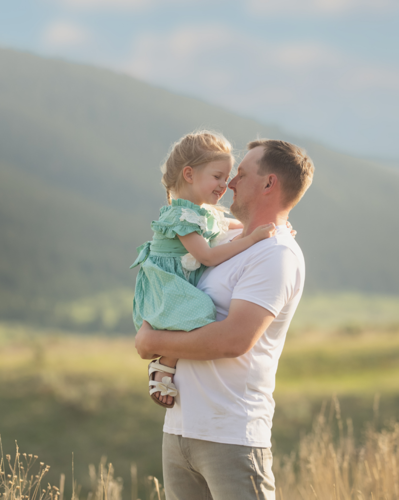 father leaning in to rub noses with daughter during family photography session, child showing genuine laughter and joy.
